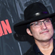 Filmmaker Robert Rodriguez wears a black hat, black shirt, and black-rimmed glasses at a Las Vegas red-carpet event.